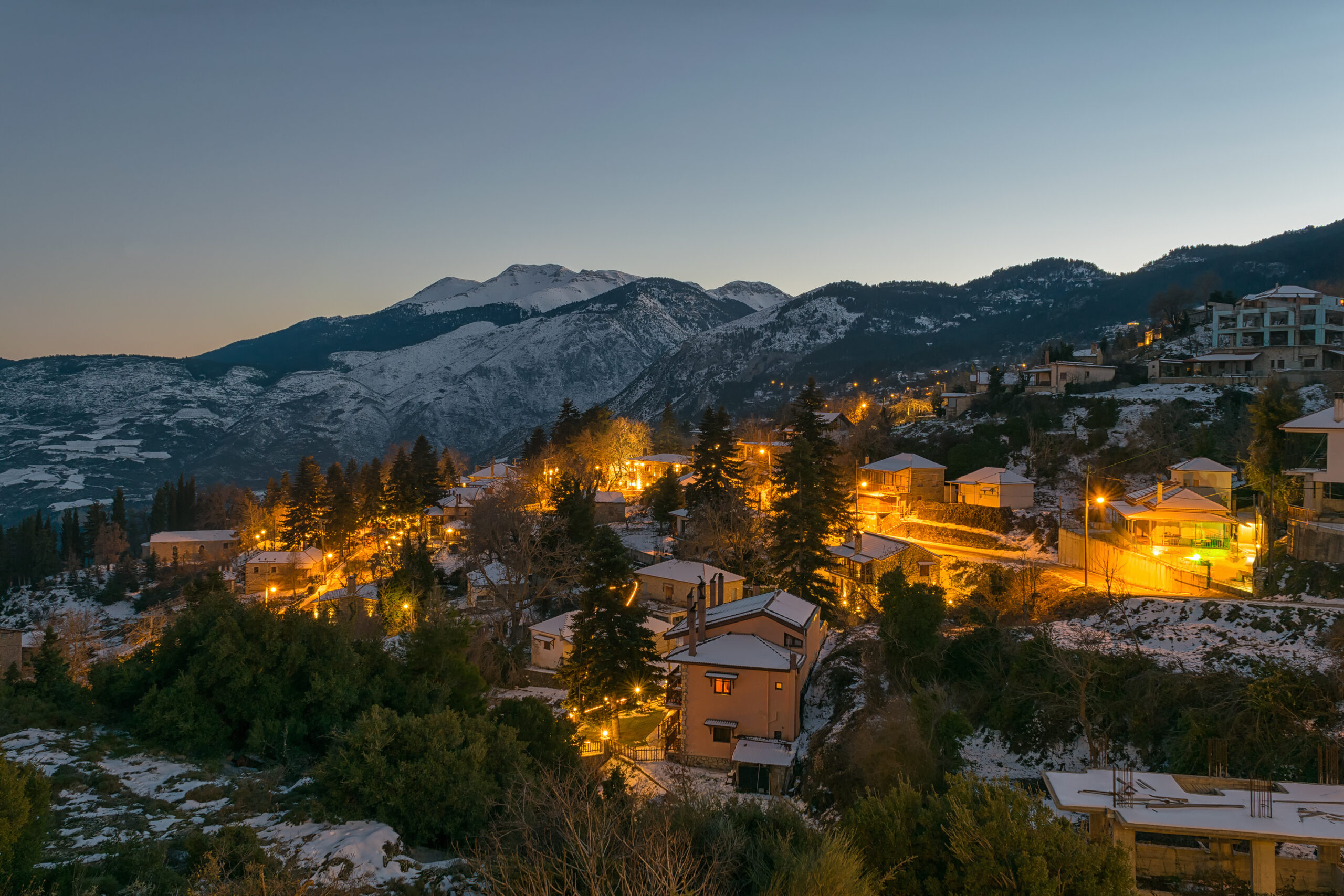 Trikala Korinthias: A Guide to the 3 Districts & Mt. Zireia 2 The lights of Mesaia Trikala, Corinthia, at dusk, with snow-covered Mount Ziria behind